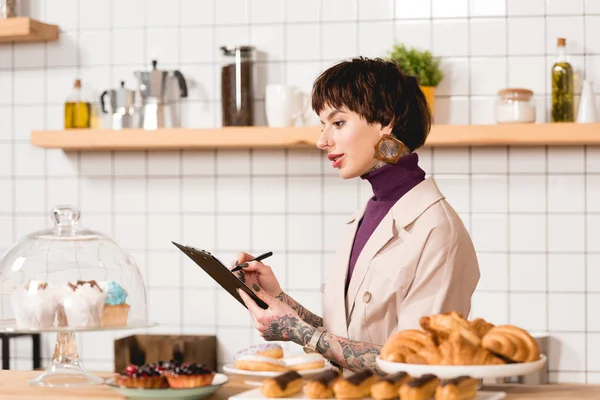 Bonita mujer de negocios escribiendo en portapapeles, mientras que de pie en el mostrador de bar en la cafetería - foto de stock