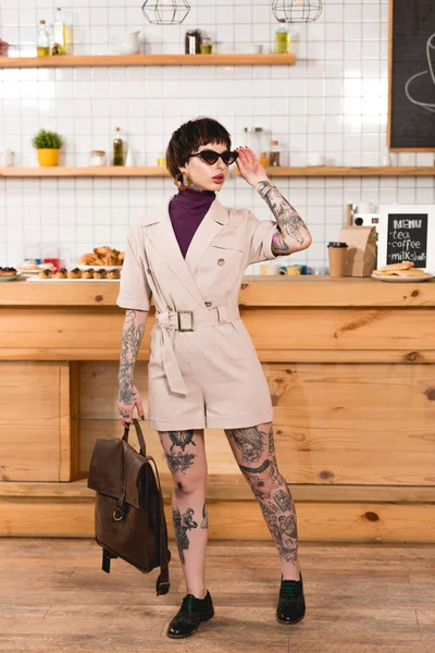 Fashionable, tattooed businesswoman in sunglasses standing at bar counter in cafeteria — Stock Photo