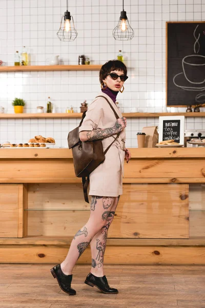 Atractiva, mujer de negocios de moda en gafas de sol de pie en el mostrador del bar en la cafetería - foto de stock