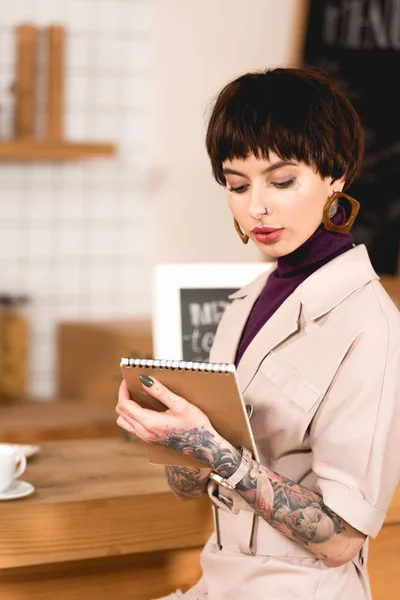 Fashionable businesswoman holding notebook while standing at bar counter in cafe — Stock Photo