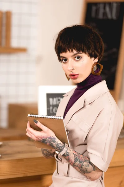 Pretty, confident businesswoman holding notebook and looking at camera — Stock Photo