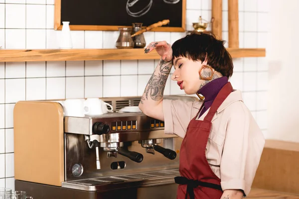 Jolie, épuisé barista debout près de la machine à expresso à la cafétéria — Photo de stock