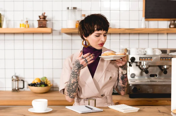 Dissatisfied businesswoman holding plate with macaroons while standing at bar counter in cafe — Stock Photo