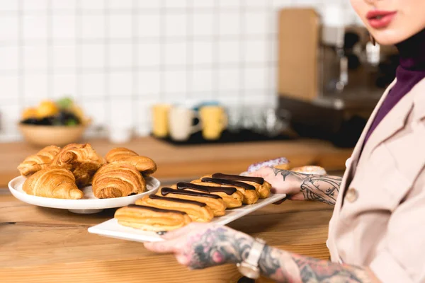 Cropped view of cafe owner placing dish with eclairs on bar counter in coffee shop — Stock Photo