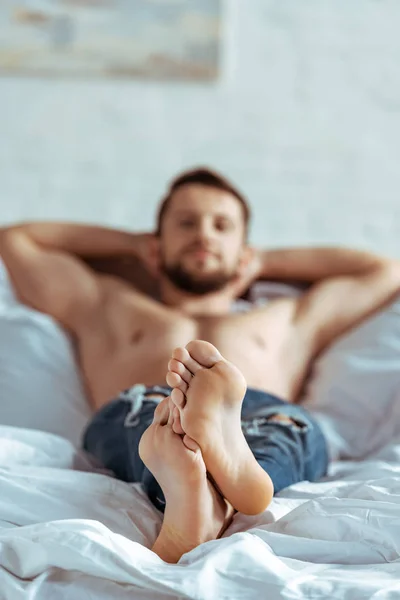 Селективное внимание привлекательного и мускулистого мужчины лежащего на кровати и смотрящего на камеру в спальне — стоковое фото