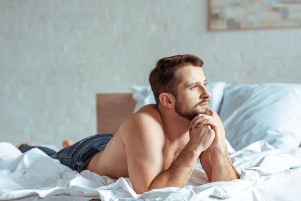 Красивый и мускулистый мужчина лежит на кровати и смотрит вдаль в спальне — стоковое фото