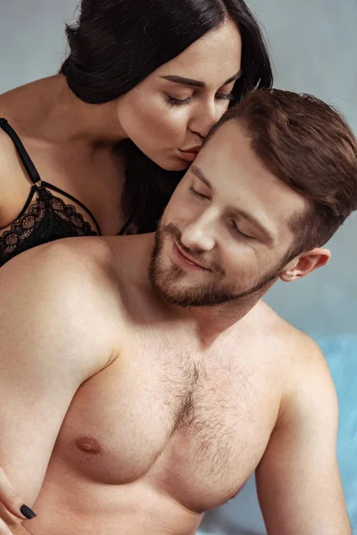 Attractive woman kissing handsome shirtless man in bedroom — Stock Photo