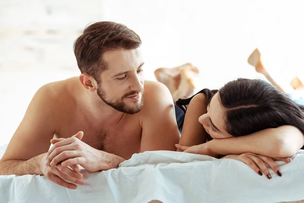 Красивый мужчина лежит на кровати и смотрит на красивую женщину в спальне — стоковое фото