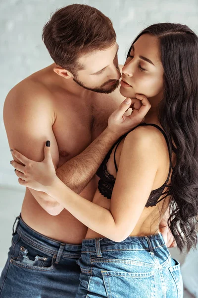 Handsome and shirtless man hugging beautiful woman in bra in bedroom — Stock Photo