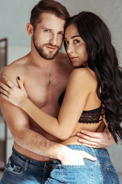 Handsome and muscular man hugging beautiful woman in bra and looking at camera — Stock Photo