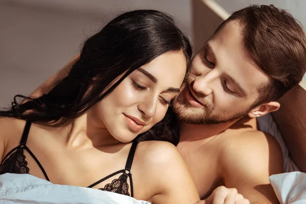 Hombre feliz y guapo abrazando a mujer hermosa y atractiva en el dormitorio - foto de stock