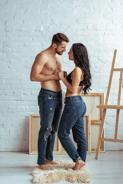 Hombre guapo y musculoso cogido de la mano con hermosa mujer en sujetador de encaje en el dormitorio - foto de stock