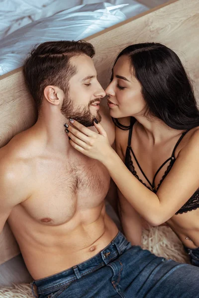 Hombre guapo y musculoso abrazos y besos con hermosa mujer en sujetador de encaje en el dormitorio - foto de stock