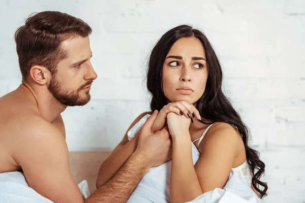 Schöner und muskulöser Mann schaut schöne und aufgebrachte Frau im Schlafzimmer an — Stockfoto