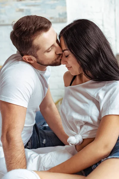 Handsome man kissing beautiful and brunette woman in bedroom — Stock Photo