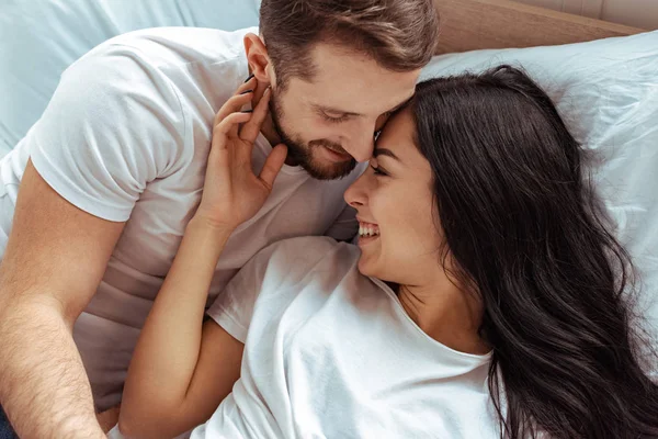 Schöner Mann umarmt schöne und lächelnde Frau in weißem T-Shirt im Schlafzimmer — Stockfoto