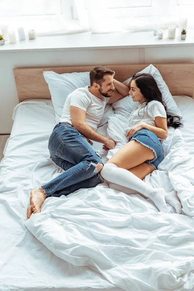 Красивий чоловік і красива і усміхнена жінка в білій футболці дивиться один на одного в спальні — стокове фото