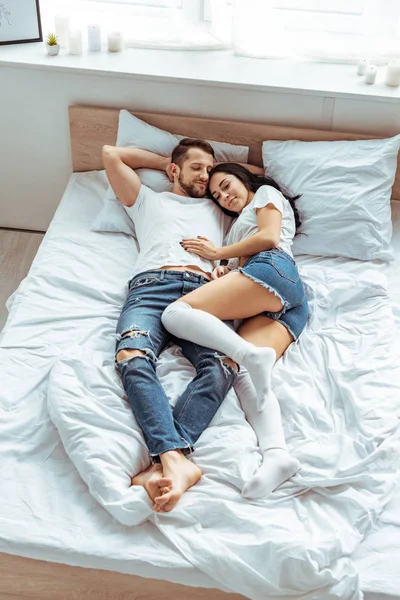 Красивий чоловік в джинсах і красива і усміхнена жінка обіймається в спальні — стокове фото
