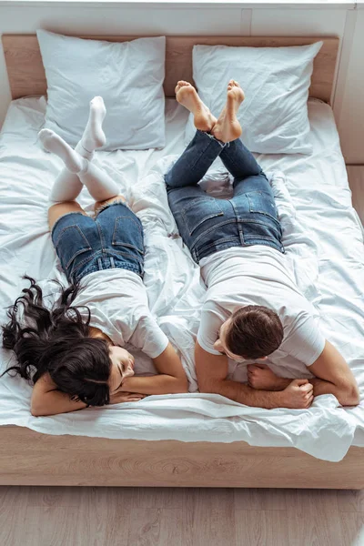 Бойфренд в джинсах и женщина в шортах и футболке лежат на кровати в спальне — стоковое фото