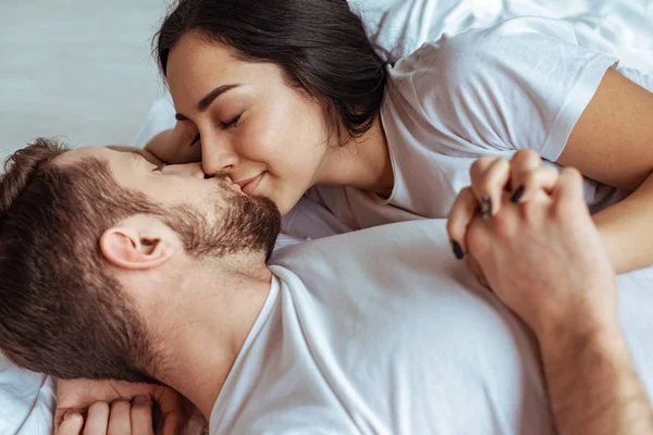 Hombre guapo y hermosa mujer acostada en la cama y besándose en el dormitorio - foto de stock