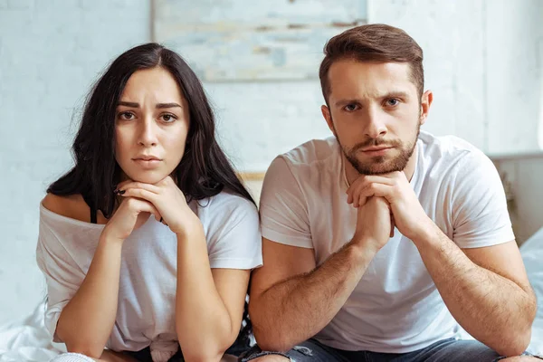 Handsome man in jeans and beautiful sad woman in t-shirt sitting on bed and looking at camera — Stock Photo
