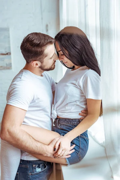 Guapo hombre abrazando hermosa y morena mujer en camiseta y pantalones cortos - foto de stock