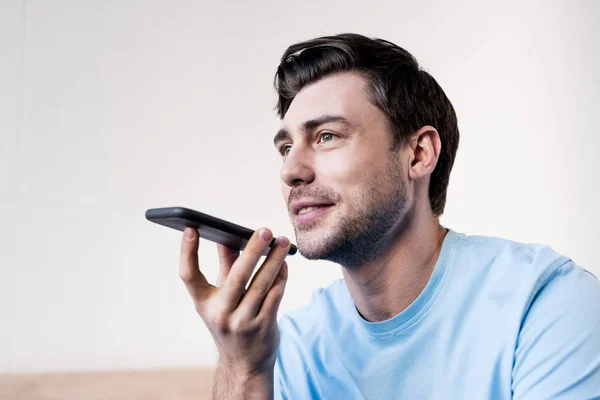 Hombre alegre en camiseta azul bostezar mientras habla en el teléfono inteligente por altavoz - foto de stock