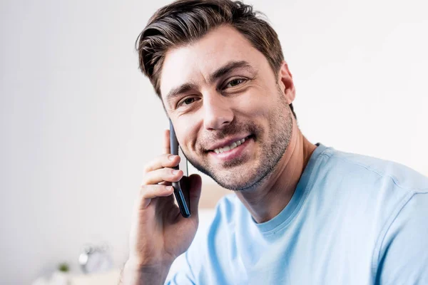 Sonriente hombre guapo hablando en el teléfono inteligente y mirando a la cámara - foto de stock
