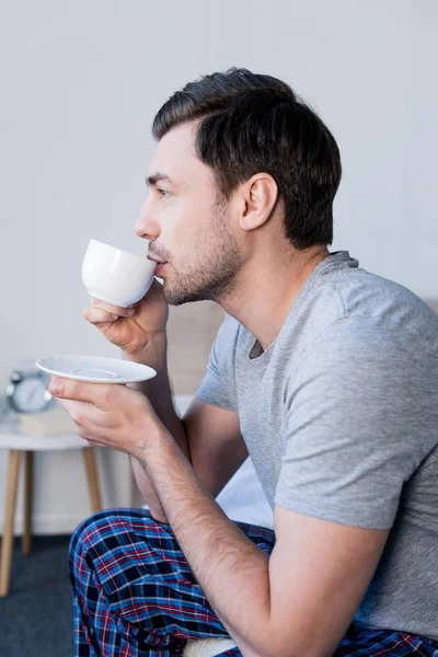 Pensive handsome man drinking morning coffee in bedroom at home — Stock Photo