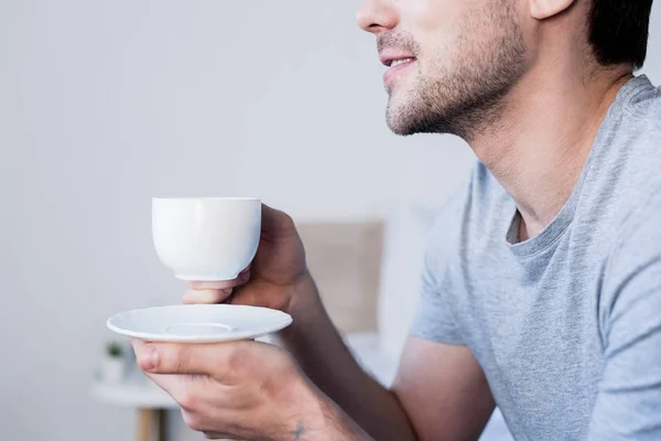 Частичный вид улыбающегося мужчины, пьющего утренний кофе в спальне — стоковое фото