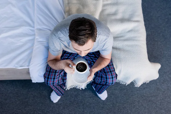 Top view of man in pyjamas holding cup of coffee while sitting on bedding — Stock Photo