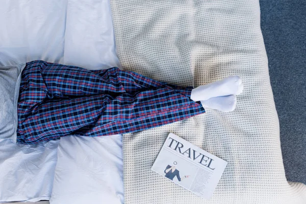 Partial view of man in pyjamas lying on bed near travel newspaper — Stock Photo