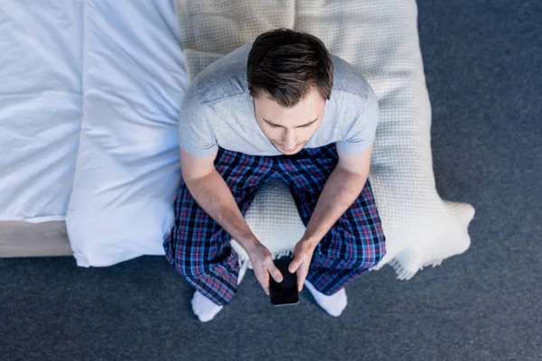 Vista superior do homem em pijama segurando smartphone com tela em branco enquanto sentado na cama em casa — Fotografia de Stock