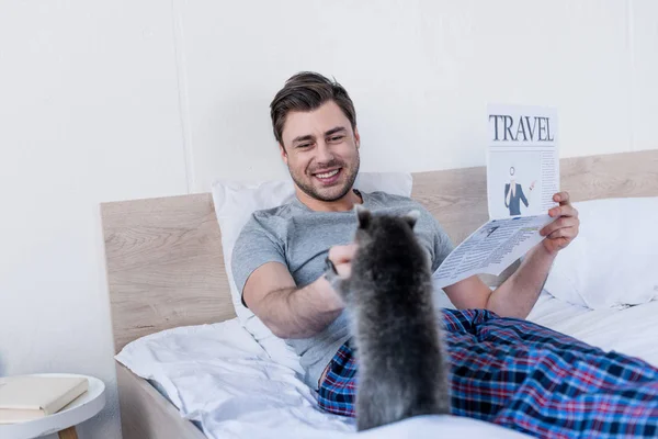 Sorrindo homem bonito jogando com guaxinim bonito enquanto segurando jornal de viagem — Fotografia de Stock