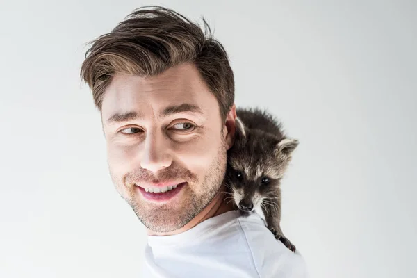 Portrait of handsome cheerful man with funny raccoon on shoulder on grey — Stock Photo