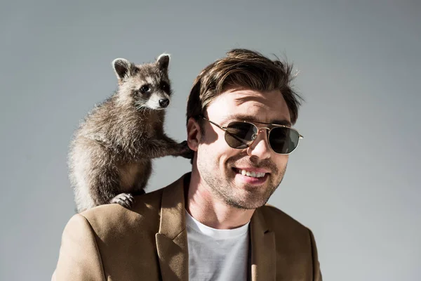 Handsome man in sunglasses with adorable raccoon on shoulder on grey — Stock Photo