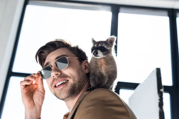 Funny raccoon sitting on shoulder of handsome smiling man in sunglasses — Stock Photo