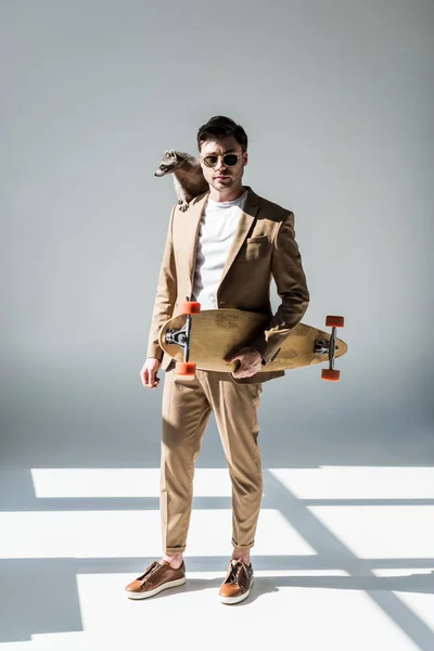 Good-looking man with funny raccoon on shoulder holding longboard and looking at camera — Stock Photo