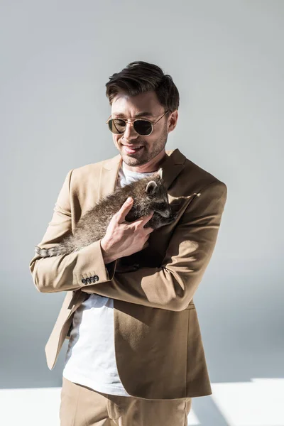 Smiling handsome man in sunglasses cuddling with adorable raccoon — Stock Photo