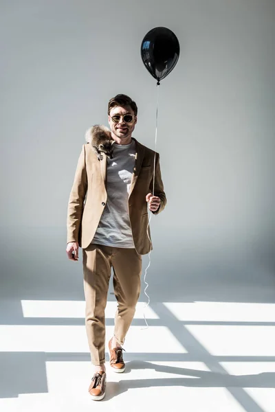 Hombre guapo alegre con mapache adorable en el hombro sosteniendo globo aéreo y mirando a la cámara — Stock Photo