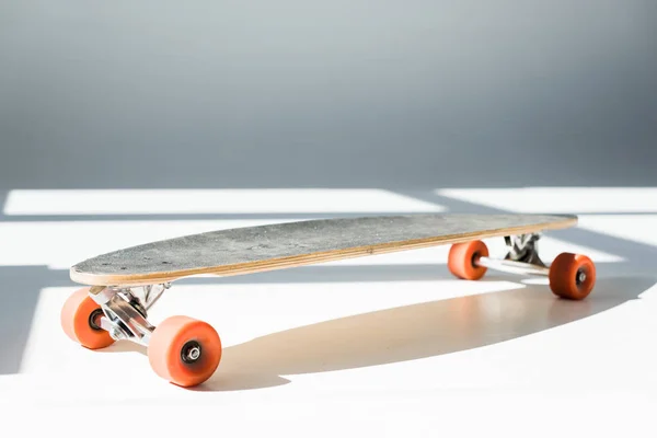 Selective focus of longboard in sunlight with shadows on grey — Stock Photo