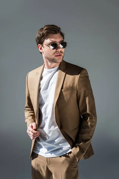 Handsome man in beige suite with hand in pocket looking away on grey — Stock Photo