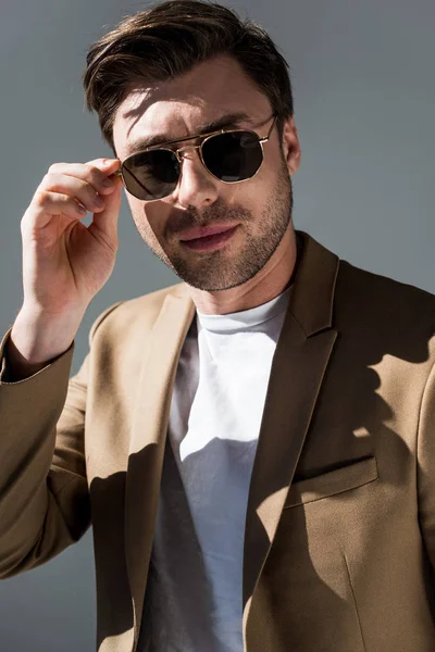 Hombre de moda con confianza en gafas de sol mirando a la cámara en gris - foto de stock