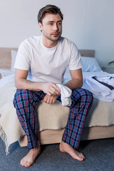 Sleepy barefoot man sitting on bedding and holding white socks — Stock Photo