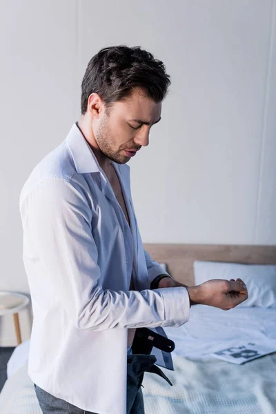 Bonito sonolento homem vestir branco camisa enquanto pé perto de cama — Fotografia de Stock