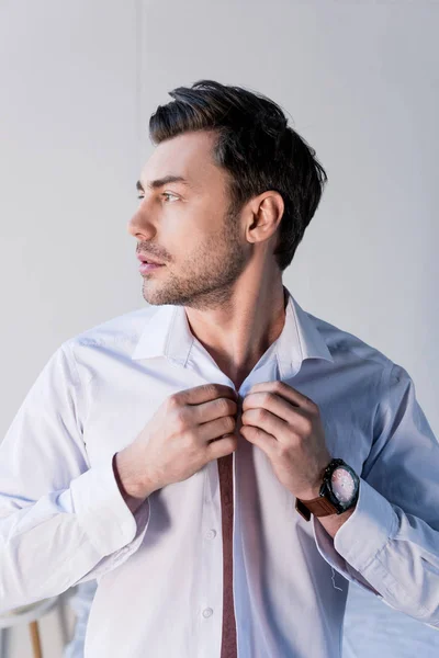 Confident handsome man putting on white shirt and looking away — Stock Photo