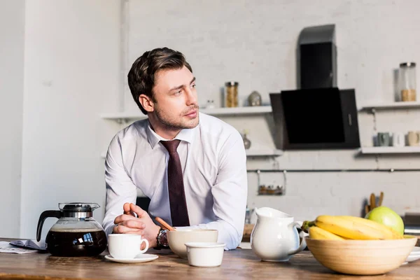 Handsome pensive man standing by kitchen table and looking away — Stock Photo
