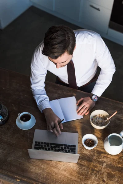 Overhead-Ansicht des Mannes mit Laptop und Notizbuch beim Frühstück zu Hause — Stockfoto