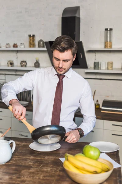 Hombre guapo en camisa blanca preparando el desayuno en la cocina en casa - foto de stock
