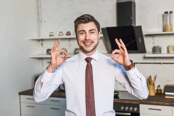 Hombre alegre de pie en la cocina en casa y mostrando signos de ok - foto de stock